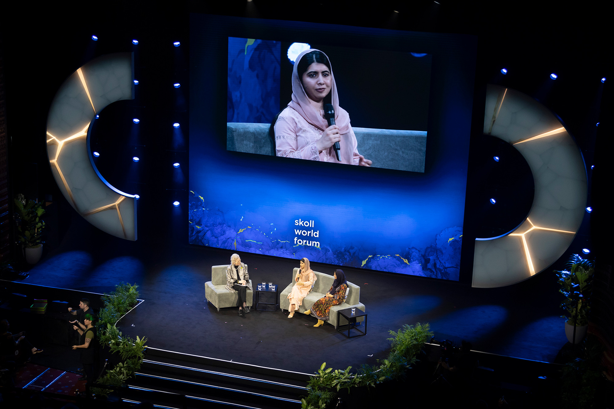 The main stage at the Skoll World Forum 2025 with two gold-veined semicircular stage pieces on either side of a live conversation