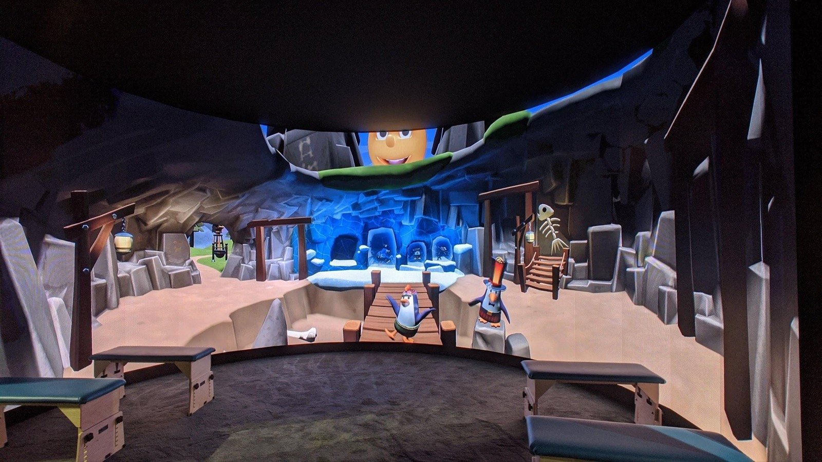 The 240 degree VR video wall curving around the booth, showing an illustrated cave environment from the therapy game library.