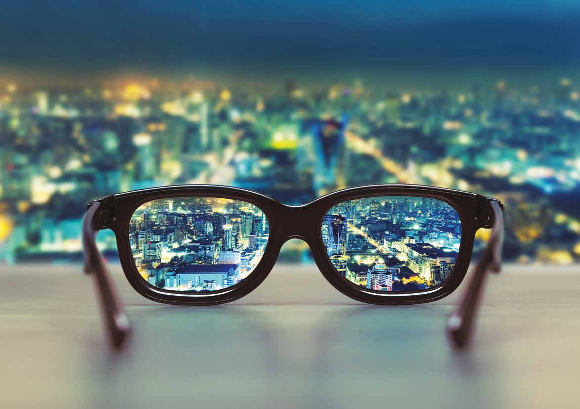 A pair of glasses on a ledge, bringing a blurred night cityscape into sharp focus through the lenses.