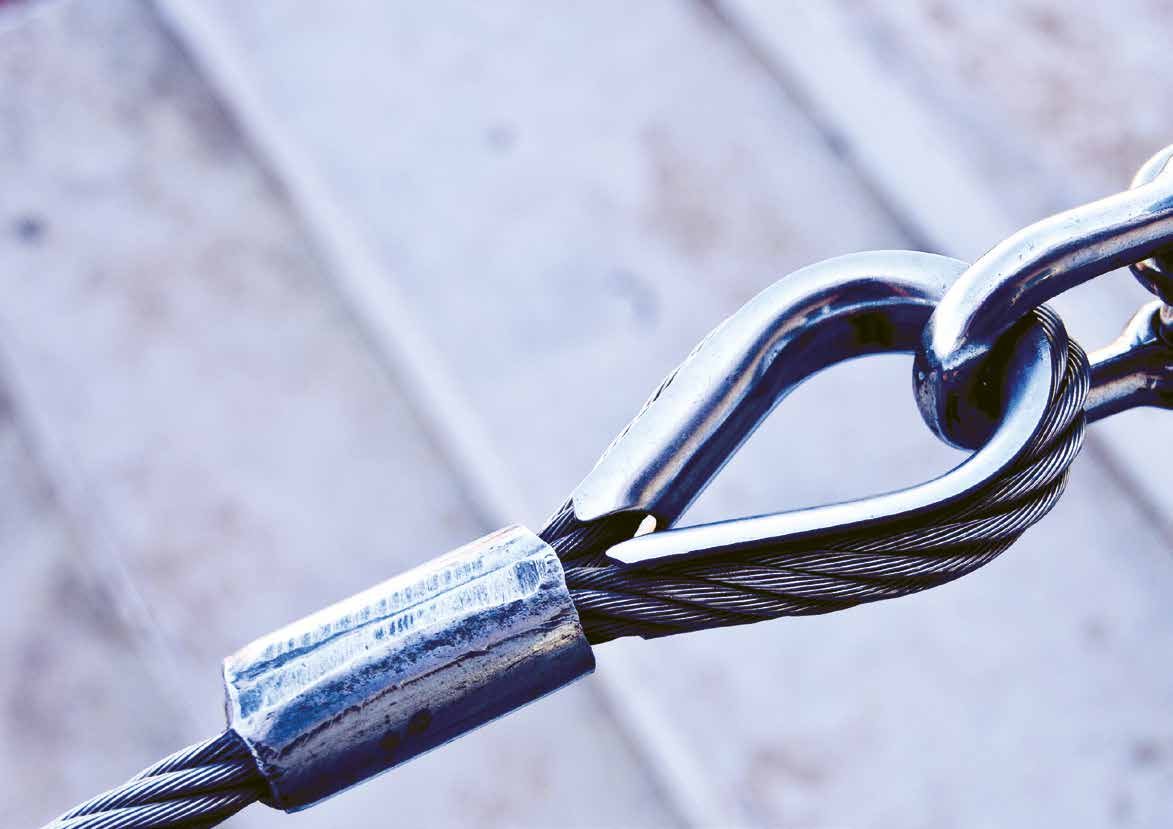 A steel cable and shackle linked tightly together against a pale weathered background.